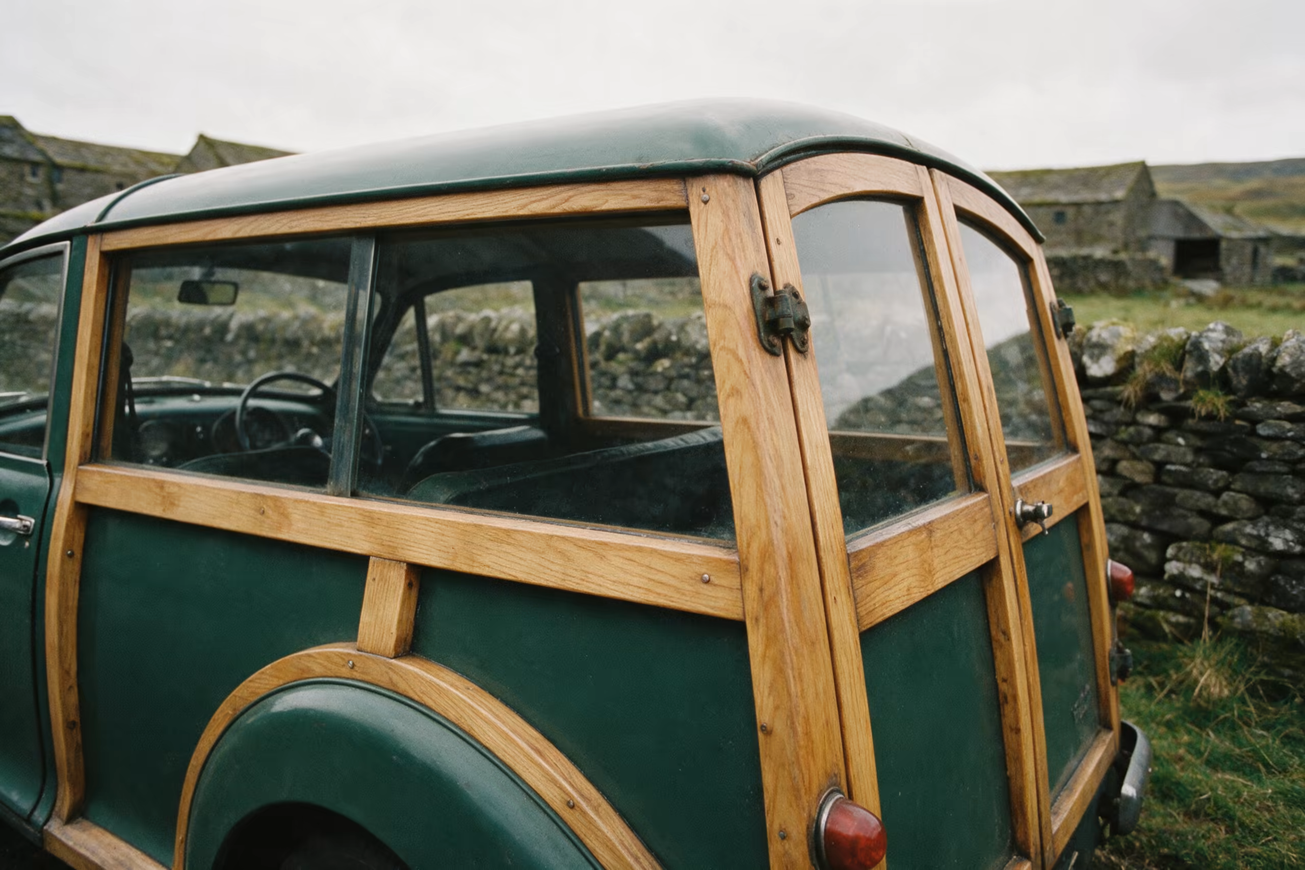 The ash timber frame and rear doors of Margaret's dark green Morris Minor Traveller, parked against a dry stone wall